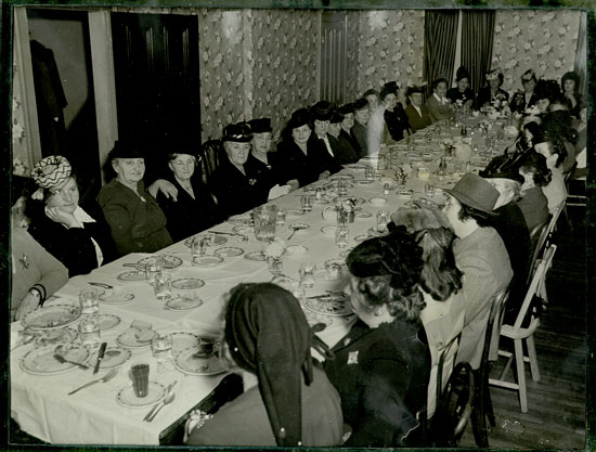 very long table with 40 or more women in sensible hats having tea