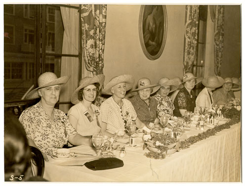 8 or more women in wide brimmed fancy hats at a fine china buffet